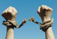 Hands breaking free from rope bindings against a clear blue sky