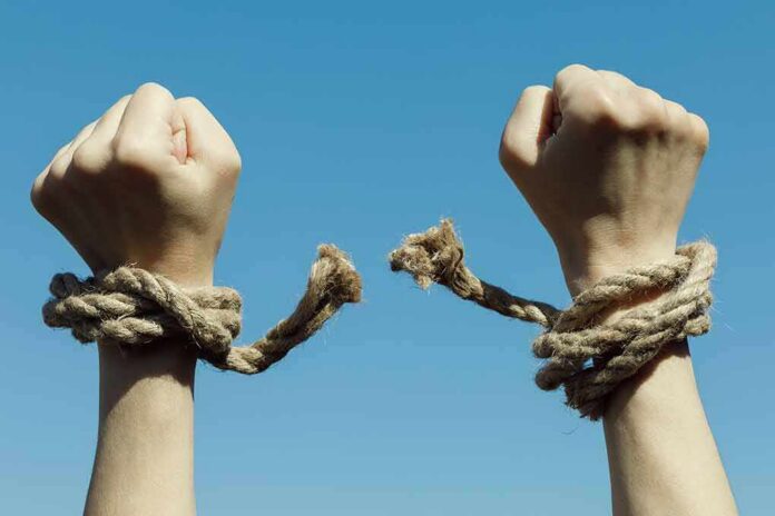 Hands breaking free from rope bindings against a clear blue sky