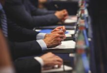 Boardroom Bombshell: Icons Expose The Real Playbook Hands of people in suits taking notes at a conference table