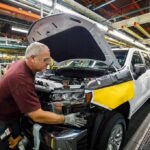 Robots Roll In After Mass Layoffs factory worker assembling a pickup truck on an automotive production line