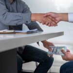 Bribed Approvals Exposed — Public Safety Risk Two people shake hands over a desk while cash is exchanged underneath