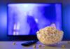 Bowl of popcorn in front of a TV with remote on table