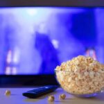 Bowl of popcorn in front of a TV with remote on table