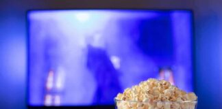 Bowl of popcorn in front of a TV with remote on table