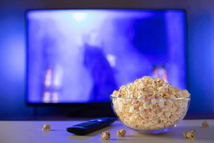 Bowl of popcorn in front of a TV with remote on table