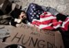 Homeless man sleeping on cardboard under an American flag