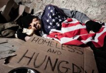 Homeless man sleeping on cardboard under an American flag