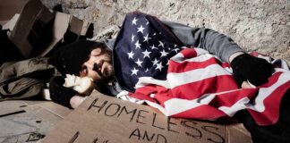 Homeless man sleeping on cardboard under an American flag