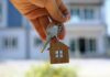 Hand holding house keys with a wooden house keychain