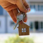 Hand holding house keys with a wooden house keychain