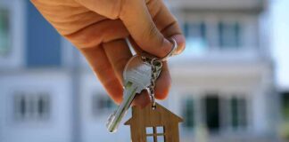 Hand holding house keys with a wooden house keychain