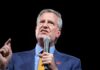 Bill de Blasio speaking into a microphone on stage