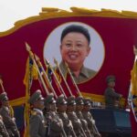 Kim Jong-il portrait banner above marching soldiers; Zhang Yufeng, Kosuke Fukudome, Hou Fenglian, Liu Guangbiao, Tsuyoshi Shinjo, Sadaharu Oh, and Lee Sang-hoon not visible