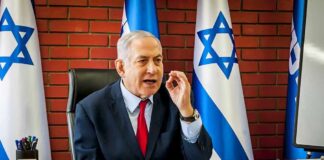 Netanyahu Slashes Trip – What Changed? man in suit speaking at a desk with Israeli flags behind him