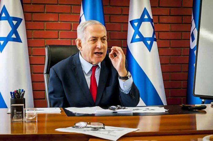 man in suit speaking at a desk with Israeli flags behind him