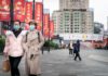 two women in face masks walking on a city plaza