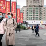 two women in face masks walking on a city plaza