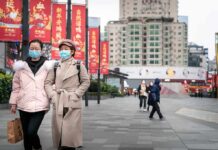 two women in face masks walking on a city plaza