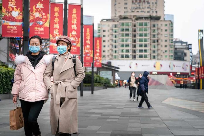 two women in face masks walking on a city plaza