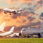 Passenger jets on airport tarmac with one aircraft landing at sunset