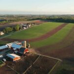 Aerial view of a farm with red barns and expansive green and brown fields