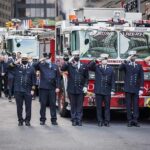 Bear Pascoe, Carlos Hyde, and Walter Jones among uniformed firefighters saluting in front of fire trucks
