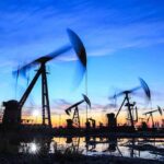 Oil pumpjacks operating at sunset over a reflective wet field