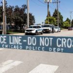 Police line barrier blocking a street with patrol vehicles behind