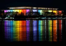 Modern building lit in rainbow colors reflected on water at night