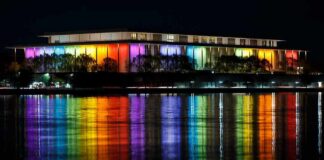 Modern building lit in rainbow colors reflected on water at night