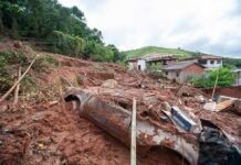 Landslide debris covering houses and a buried car on a muddy hillside
