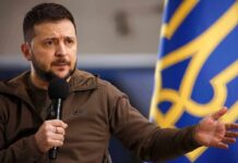 Kyiv Agencies Collide: Zelensky SLAMS ‘Disgrace’ Shootout man speaking into a microphone with hand gesturing