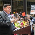 Warrants Ignored — Families Pay the Price Speaker at a podium addressing a crowd with microphones and protest signs