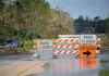Road closed barricades blocking a flooded rural highway with detour sign
