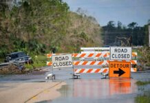 Road closed barricades blocking a flooded rural highway with detour sign