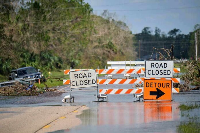 shutterstock_2211945721 Road closed barricades blocking a flooded rural highway with detour sign