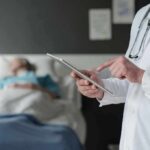 Horrific Drug Swap Maims Surgery Patients Doctor using tablet beside hospital patient