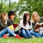Group of young women reading books on grass in a park