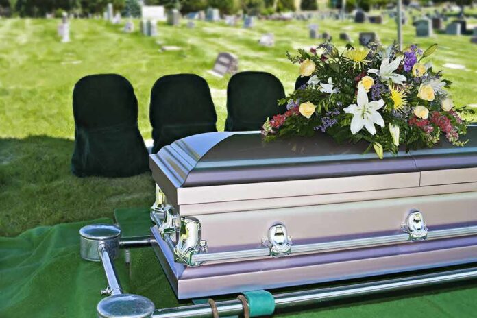 casket with floral arrangement at outdoor graveside service