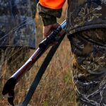 Hunter in camouflage holding a rifle in tall grass