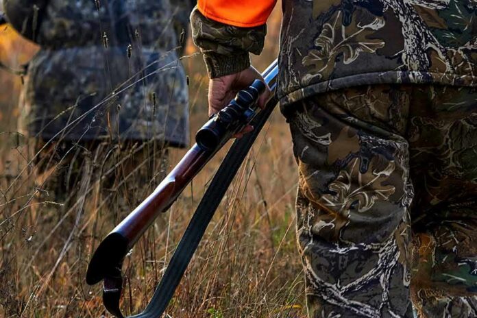 Hunter in camouflage holding a rifle in tall grass