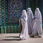 Three women in white veils walking past ornate blue tilework
