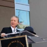 Bill Maher speaks at a podium during an outdoor event