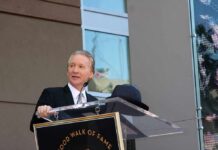 Bill Maher speaks at a podium during an outdoor event