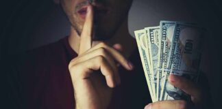 Person holding US dollar bills while making a shushing gesture