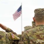 Soldiers in camouflage uniforms salute a U.S. flag