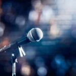 Crowd ERUPTS After Seinfeld’s Razor-Edge Comeback microphone on a stand with blurred stage lights