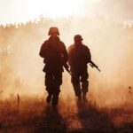 Two soldiers walking through a smoky field at sunset