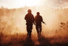 Two soldiers walking through a smoky field at sunset