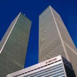 Twin rectangular skyscrapers rising above a hotel facade against a clear blue sky